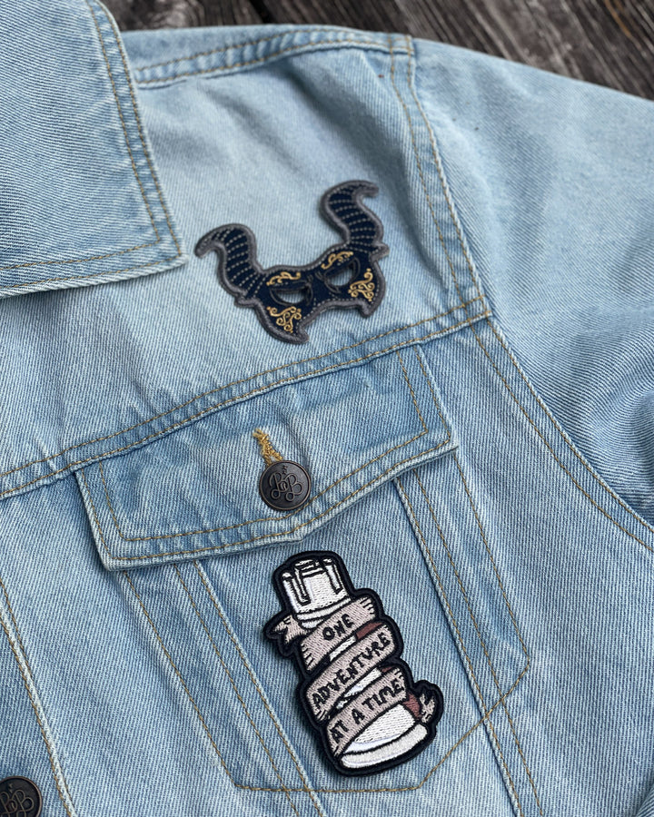 VE Schwab patch set for A Darker Shade of Magic fans featuring two patches, one designed to be a blue and gold masquerade mask, the other featuring a rook with a banner wrapped around it with the phrase &