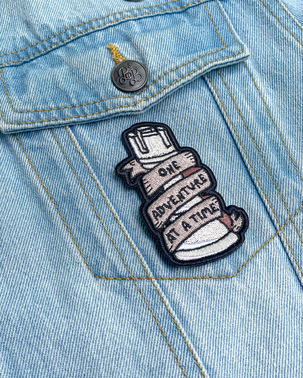 ADSOM patch of a rook with a banner wrapped around it featuring the quote 'One adventure at a time' on it.