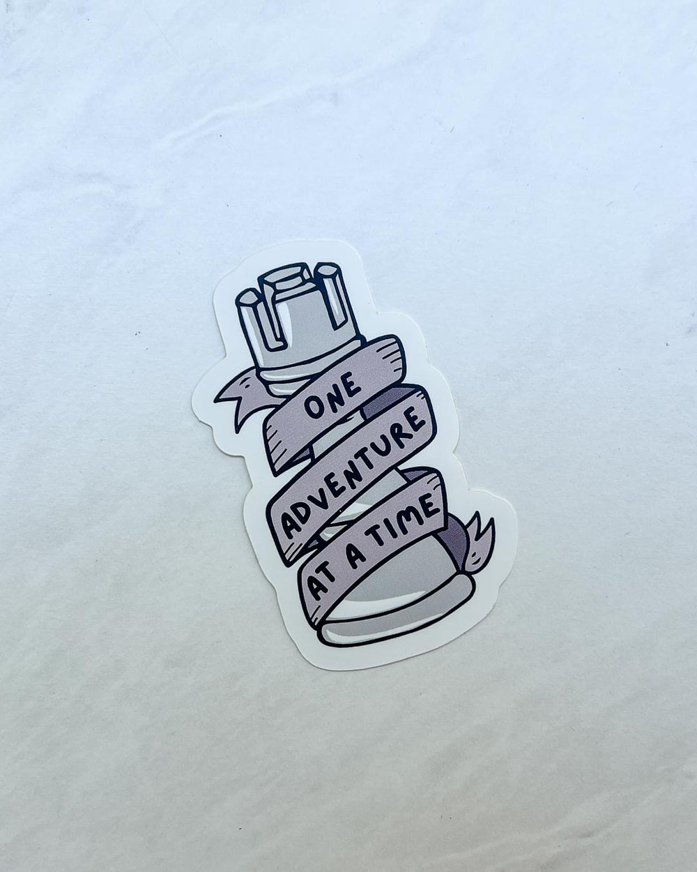 ADSOM sticker featuring an illustrated rook with a banner wrapped around it spelling out 'One adventure at a time.'