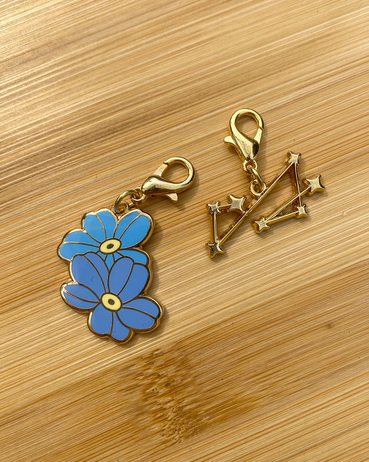 Addie LaRue charms featuring two forget me nots and a seven pointed constellation.