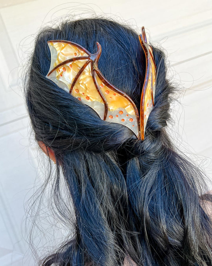 Hair combs for dragon lovers featuring two large combs in the shape of dragon wings with engraved details and a pearlescent gold color.