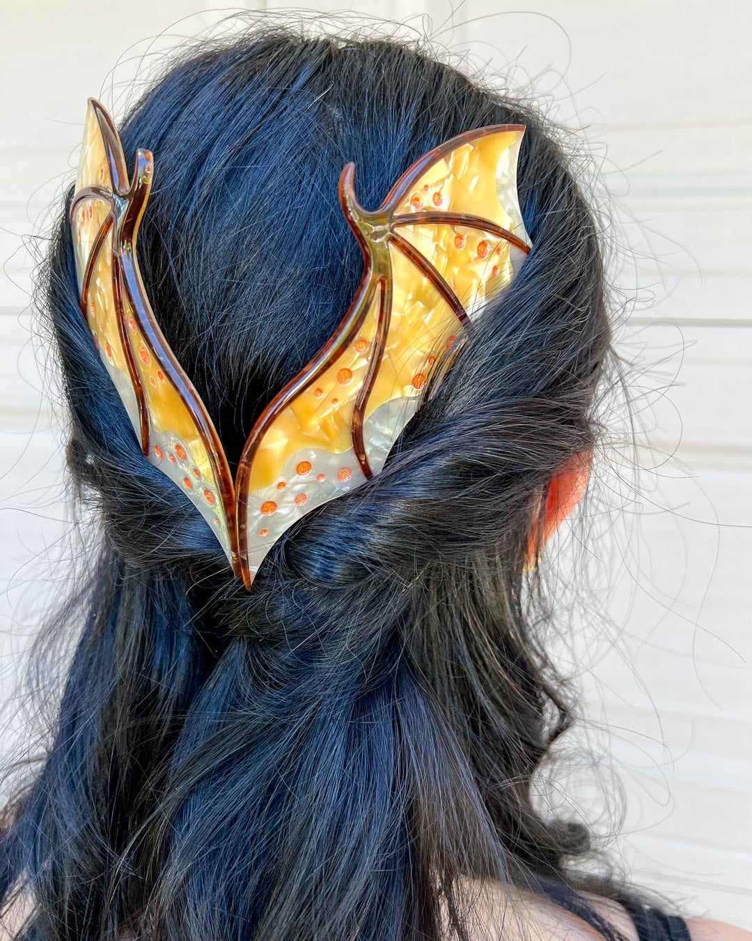 Hair combs for fantasy fans featuring two gold combs in the shape of dragon wings with engraved embellishments and a pearlescent gold color.