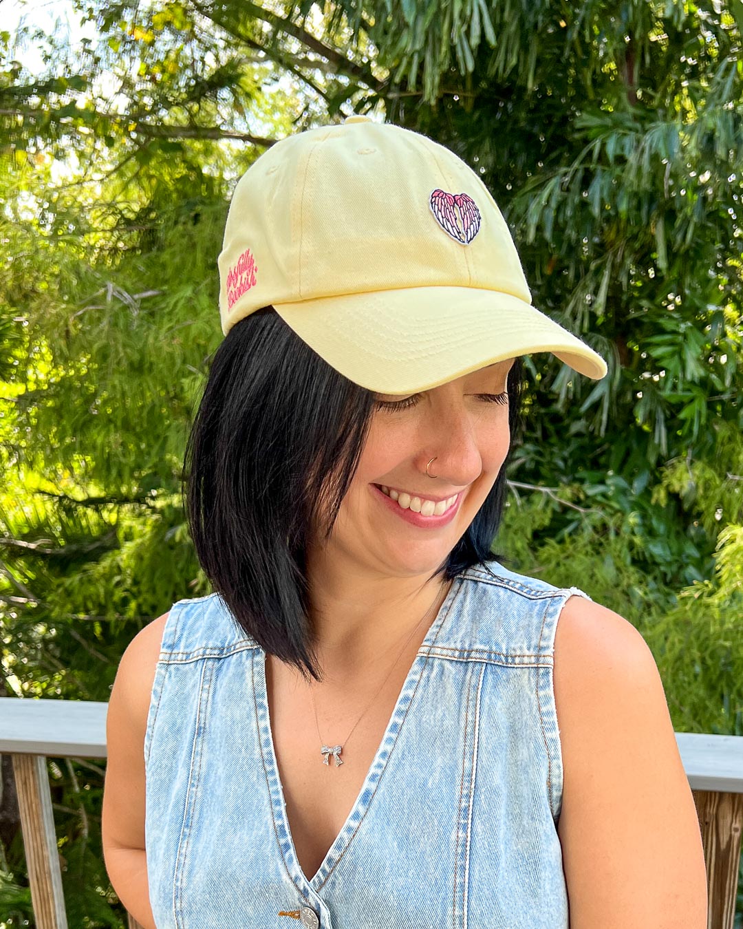 Light yellow fantasy hat featuring a patch with angel wings on it worn by a woman outdoors.