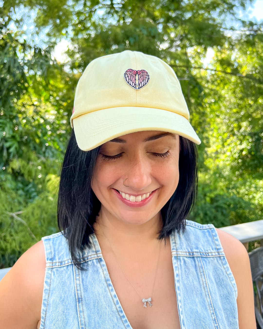 Person wearing a light yellow cap with an angel wings design for fantasy readers outdoors.