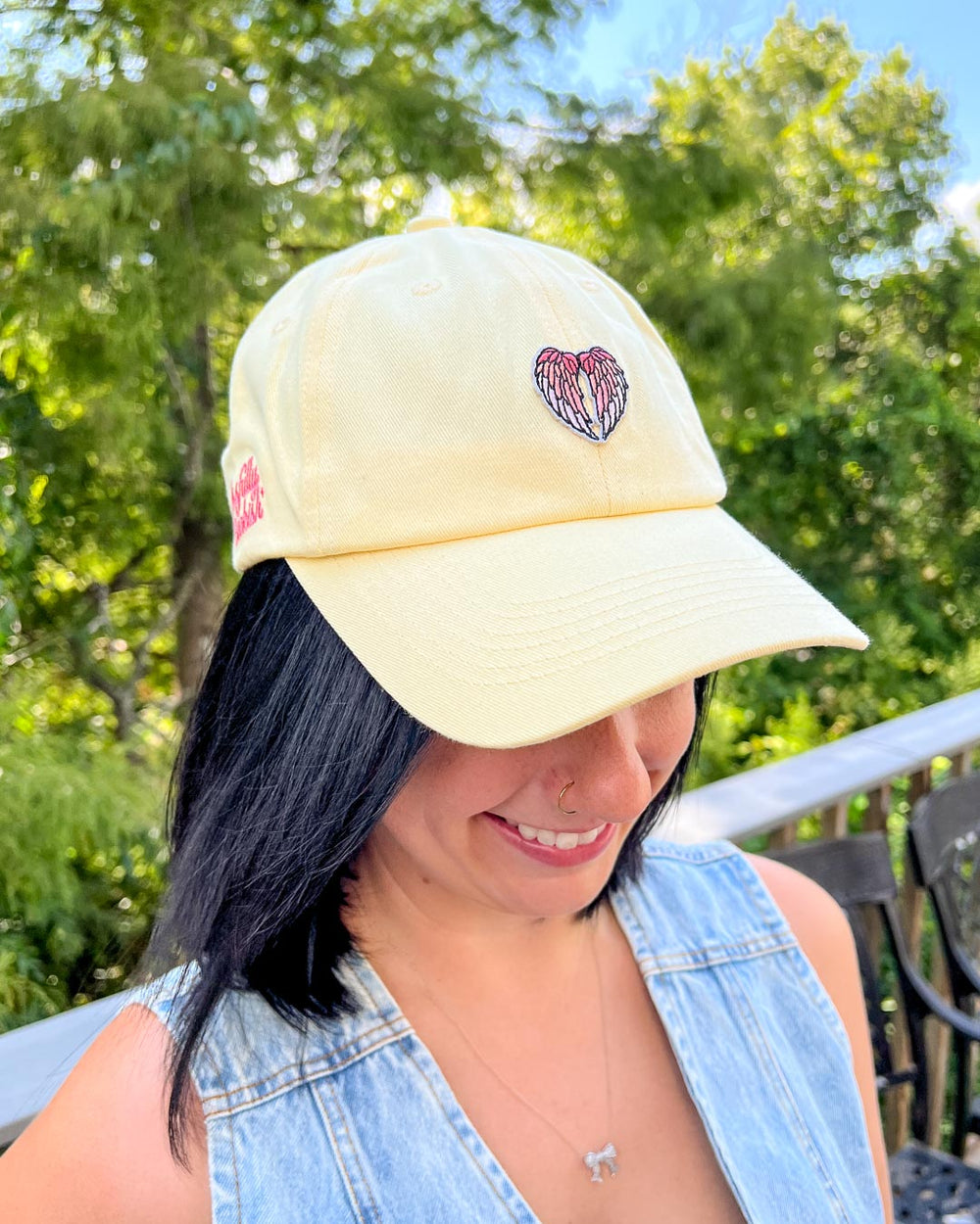 Woman wearing a yellow baseball hat for romantasy fans featuring a pink gradient angel wings patch.