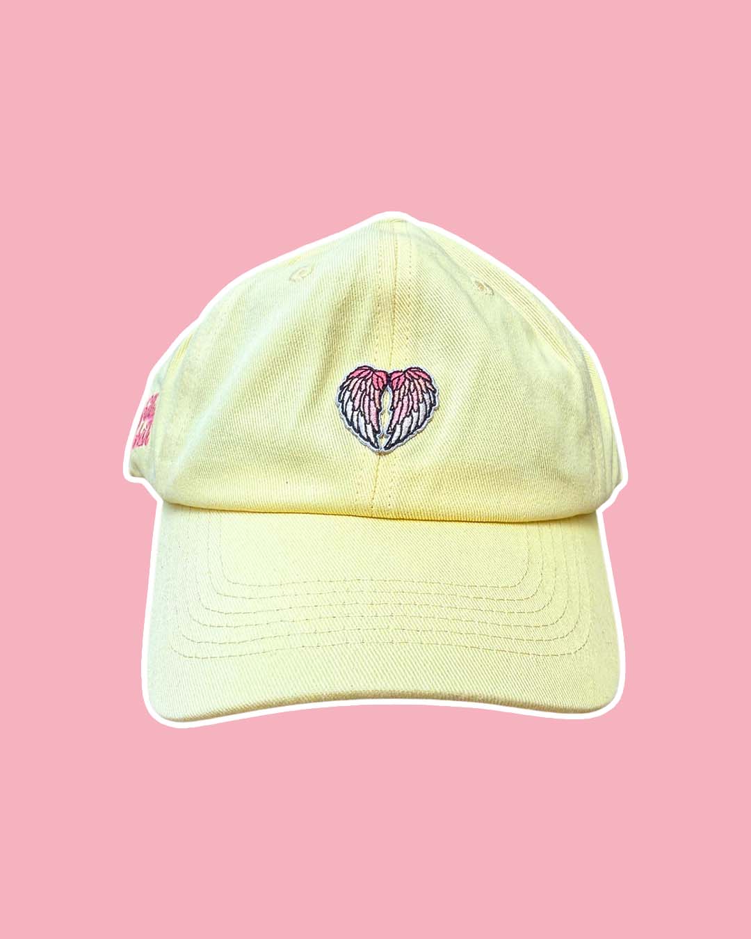Yellow minimalist hat with an ombre pink angel wings patch on the front on a pink background.