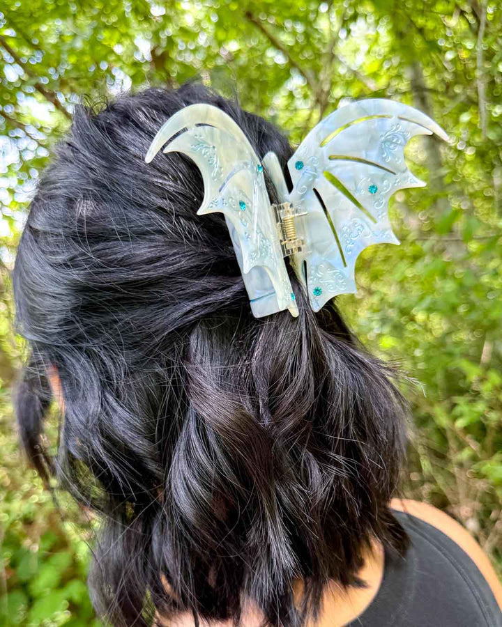 ACOTAR hair clip in the shape of bat wings in a pastel blue pearlescent design with etchings and blue gem embellishments.