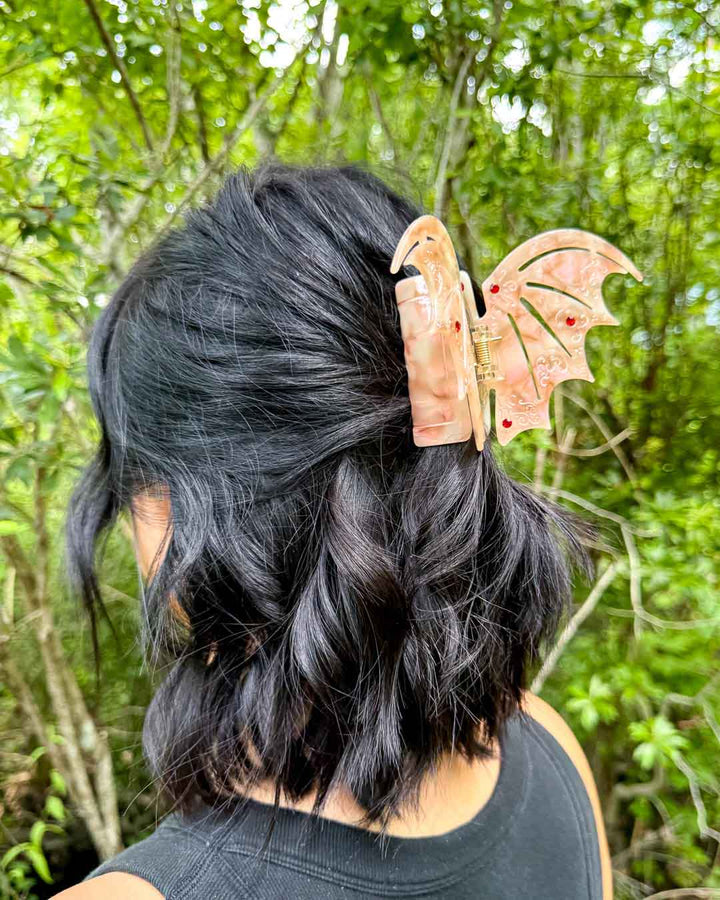 ACOTAR hair clip in the shape of bat wings in a pastel red pearlescent design with etchings and red gem embellishments.