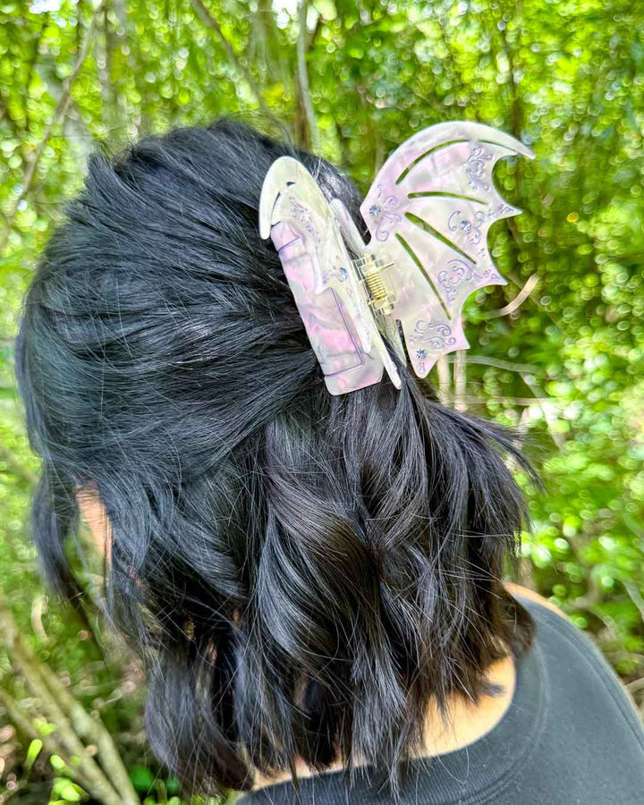 ACOTAR hair clip in the shape of bat wings in a pastel purple pearlescent design with etchings and purple gem embellishments.