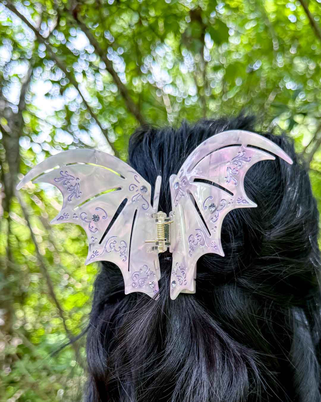 A pearlescent bookish hair clip in pastel purple with purple gem embellishments in the shape of bat wings inspired by ACOTAR.