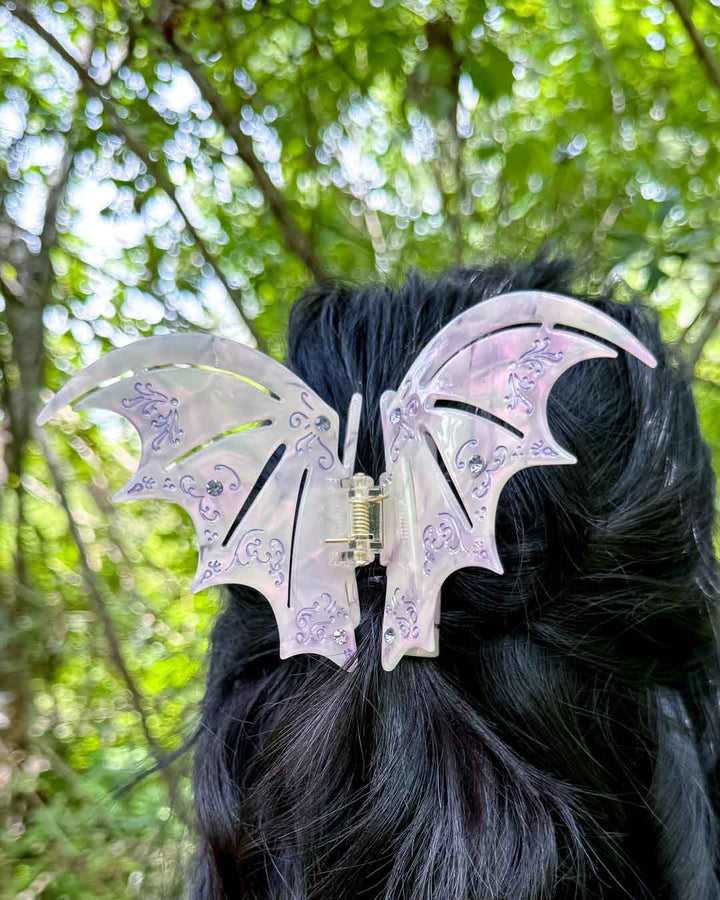 A pearlescent bookish hair clip in pastel purple with purple gem embellishments in the shape of bat wings inspired by ACOTAR.