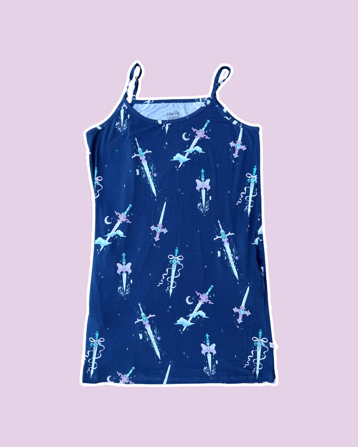 Plain purple background with blue fantasy nightgown with spaghetti straps featuring different whimsical daggers with gems, butterflies, bows, clouds, and crescent moons.