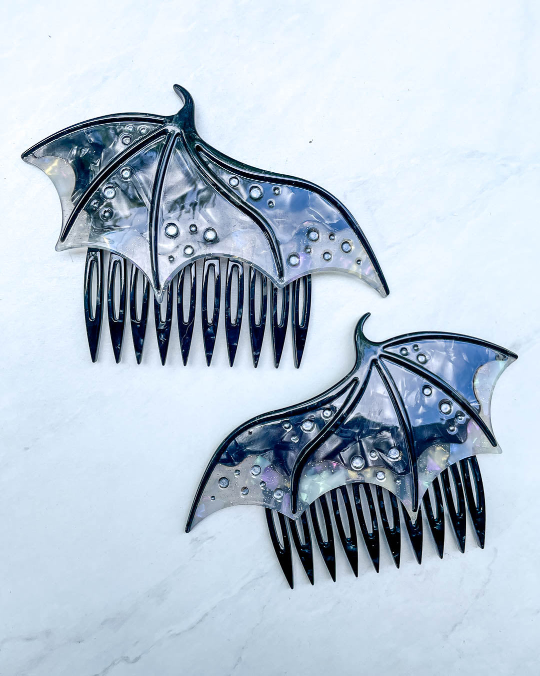 Hair combs for fantasy fans featuring two black combs in the shape of dragon wings with engraved embellishments and a pearlescent black color.