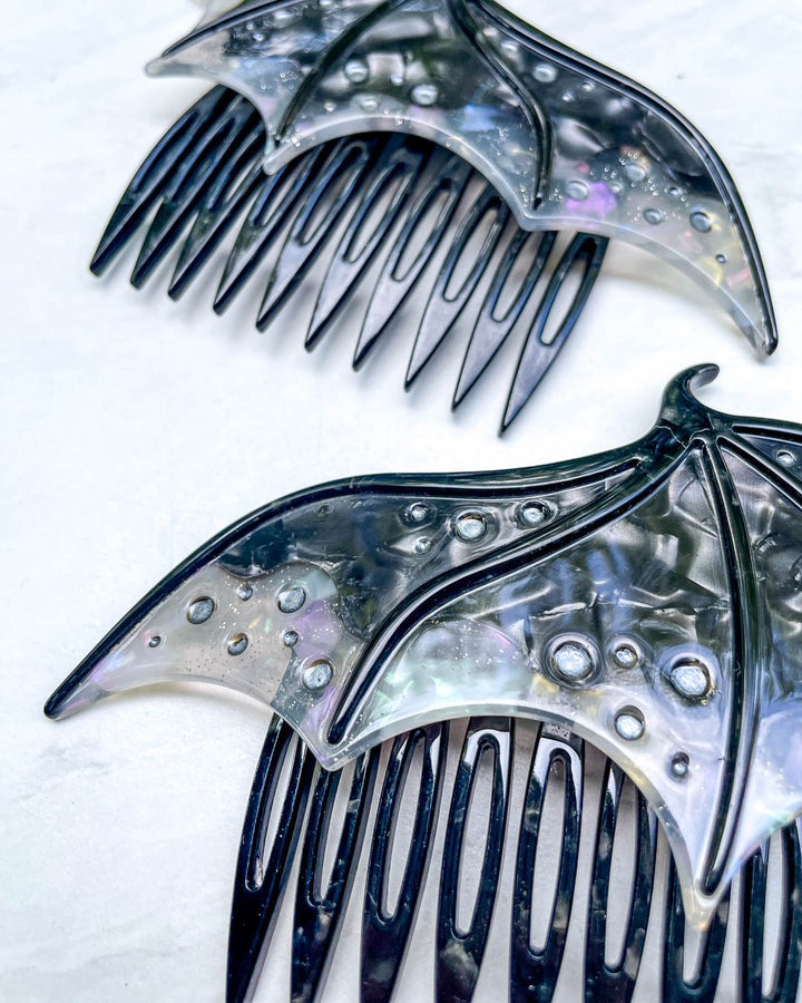 Close up of a fantasy hair accessory in the shape of dragon wings, featuring two combs in a black pearlescent color and engraved details.