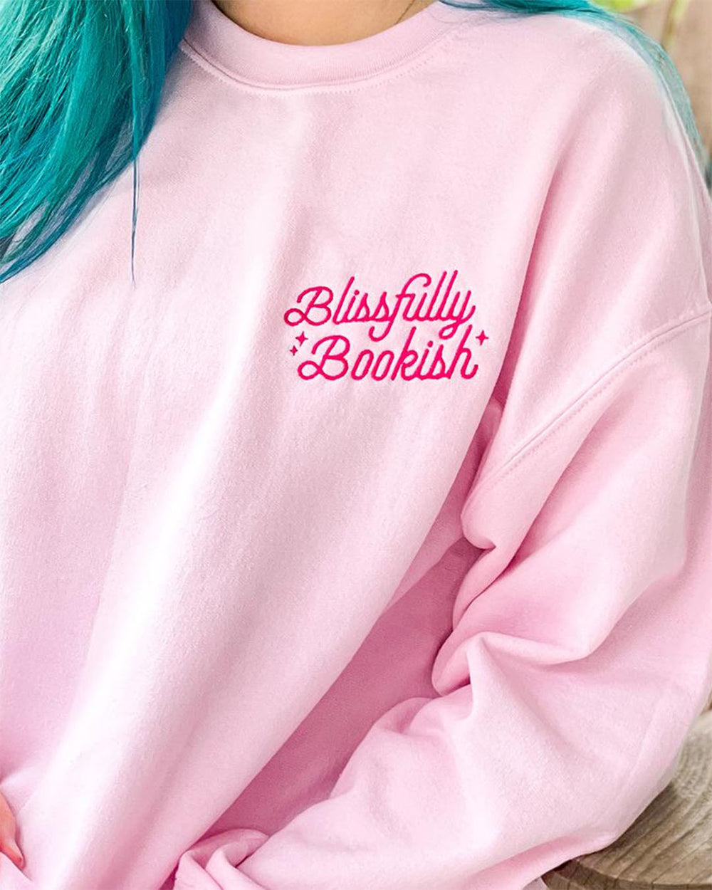 Embroidered sweatshirt in light pink with the Blissfully Bookish logo written in hot pink on the left chest.