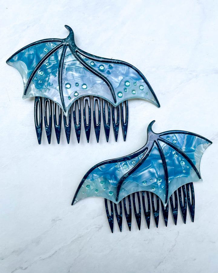 Hair combs for fantasy fans featuring two blue combs in the shape of dragon wings with engraved embellishments and a pearlescent blue color.
