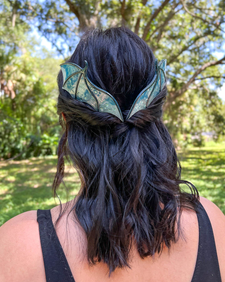 Fantasy hair combs featuring large combs in the shape of dragon wings in blue with engraved embellishments and a pearlescent color.