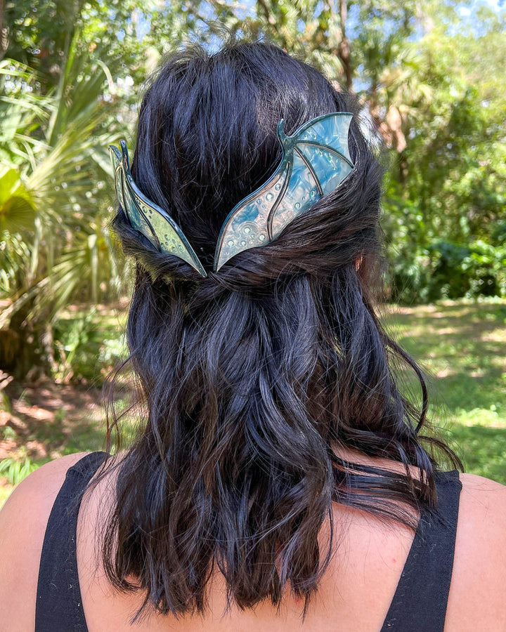 Hair combs for dragon lovers featuring two large combs in the shape of dragon wings with engraved details and a pearlescent blue color.