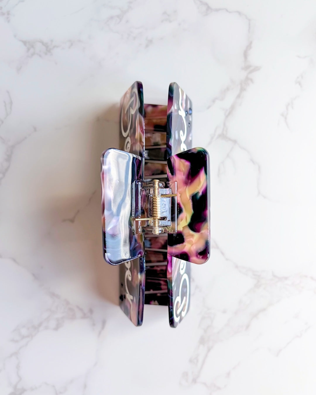 Top of a marbled claw clip for book lovers showing a gold hinge on a white marbled countertop background.