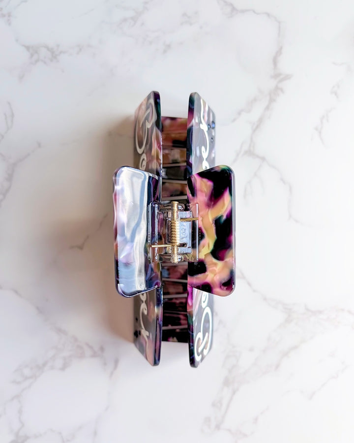 Top of a marbled claw clip for book lovers showing a gold hinge on a white marbled countertop background.