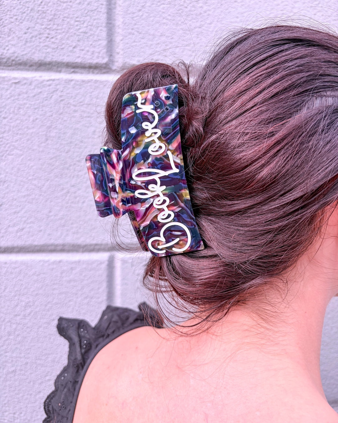 Close up of woman wearing a hair clip for readers with a dark, multi-colored marble design with "Book Lover" etched in white.