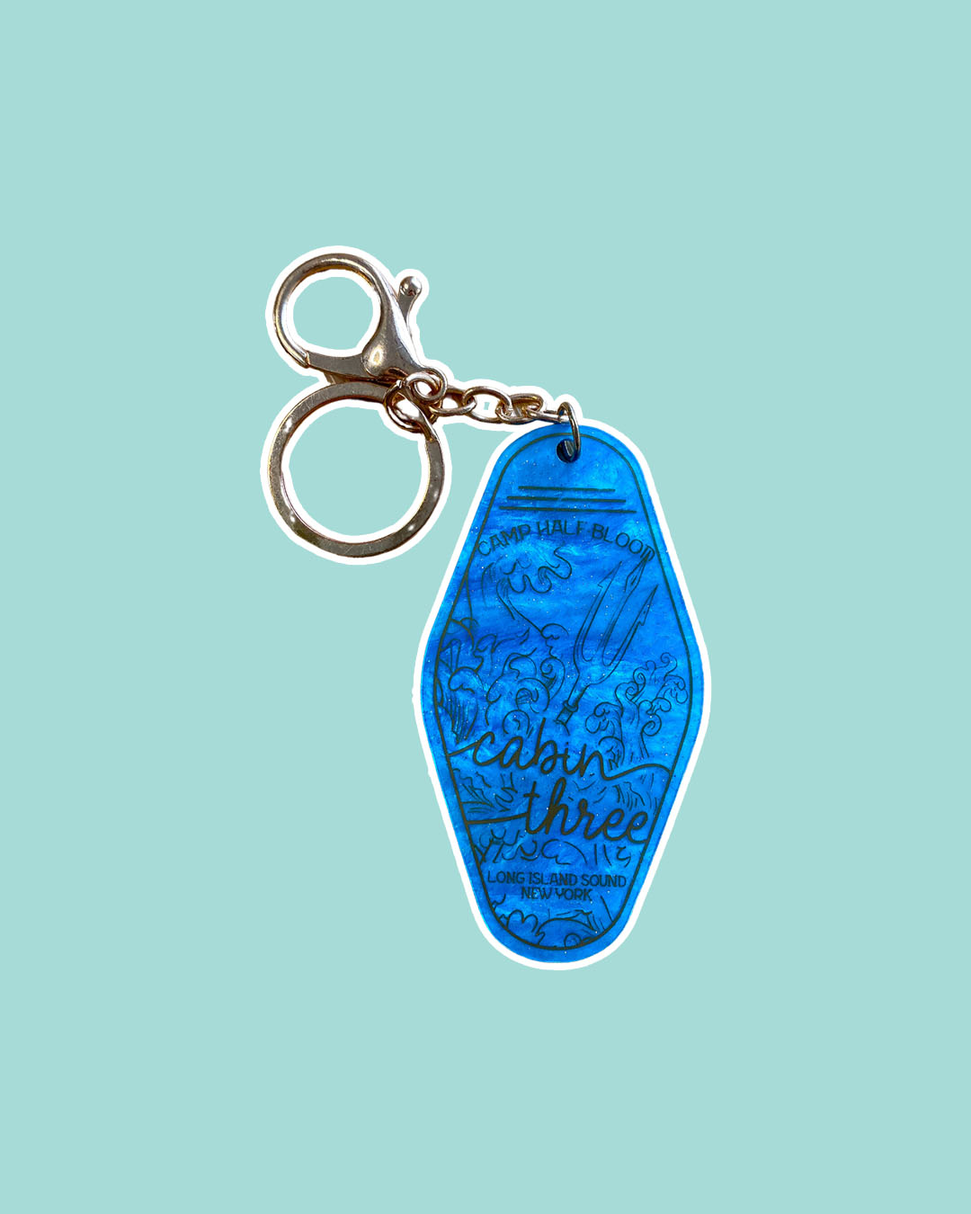 PJO keychain featuring a design for a motel key for Cabin Three, including illustrated waves and a trident. 