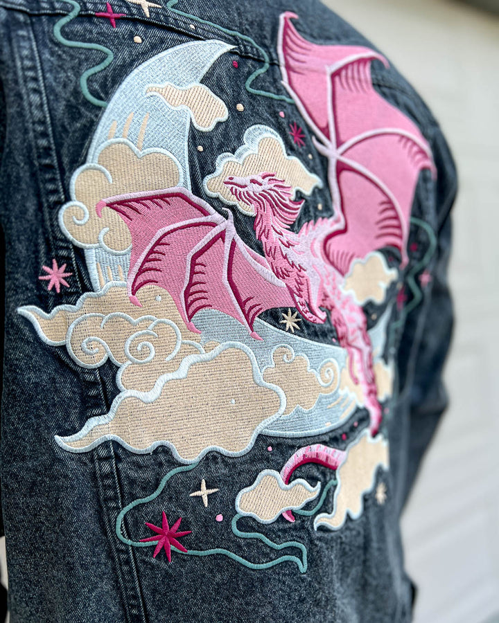 Celestial dragon oversized jean jacket with a vibrant embroidered design of a pink flying dragon over a crescent moon amongst stars and clouds.