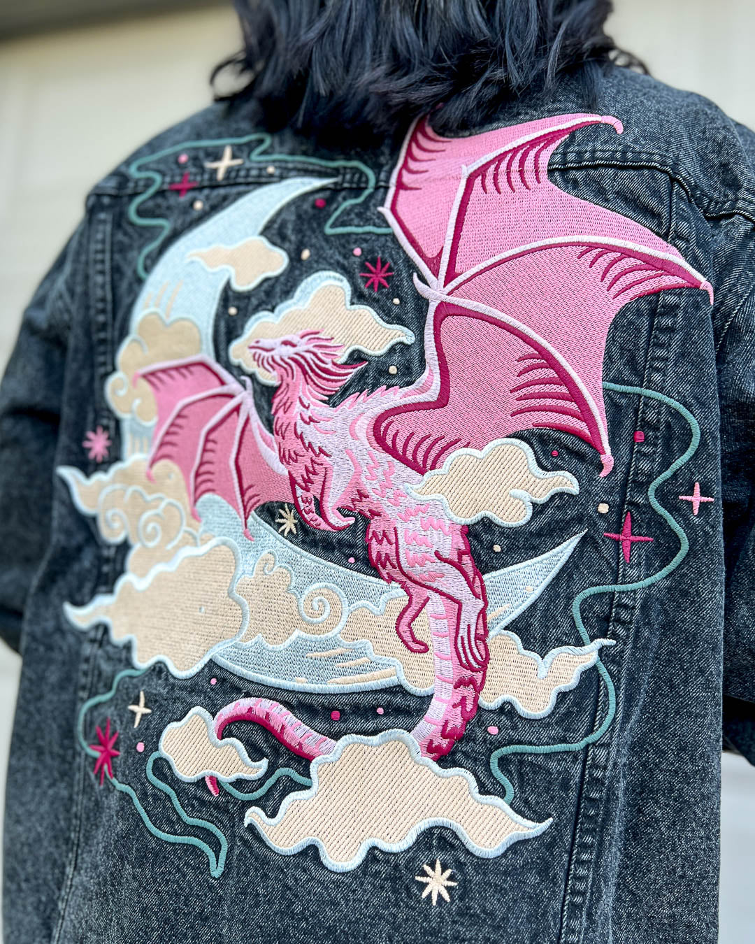 Celestial dragon oversized denim jacket featuring a colorful embroidered design of a dragon flying through clouds and stars in front of a crescent moon.