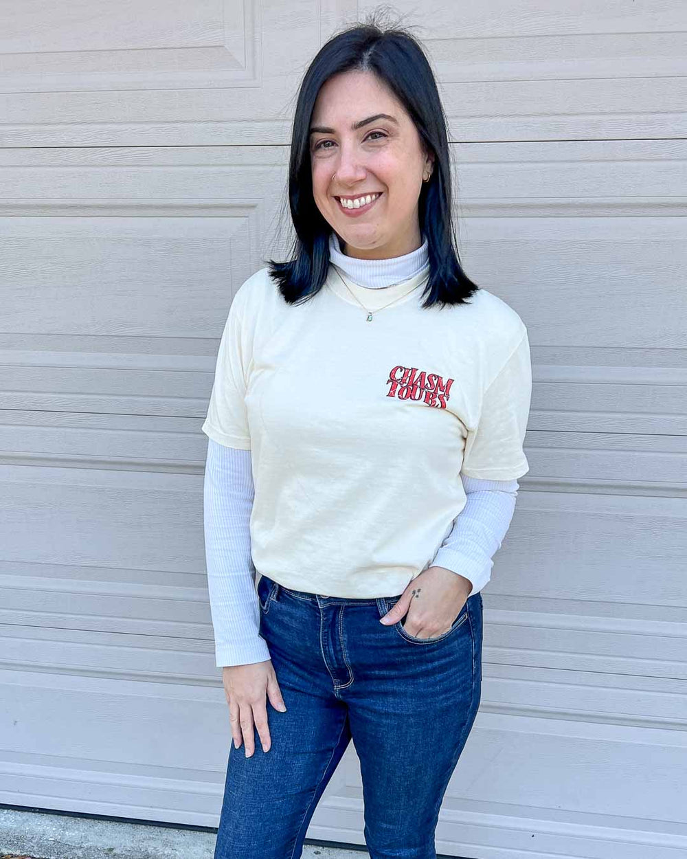 Woman wearing an ivory shirt with "Chasm Tours" written in capital, red, distressed letters on the top left chest.