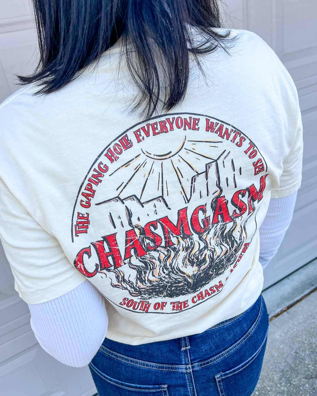 Close up of the back of the Chasm Tours ivory shirt, featuring a circular logo of the chasm that reads "Chasmgasm" in distressed red text.