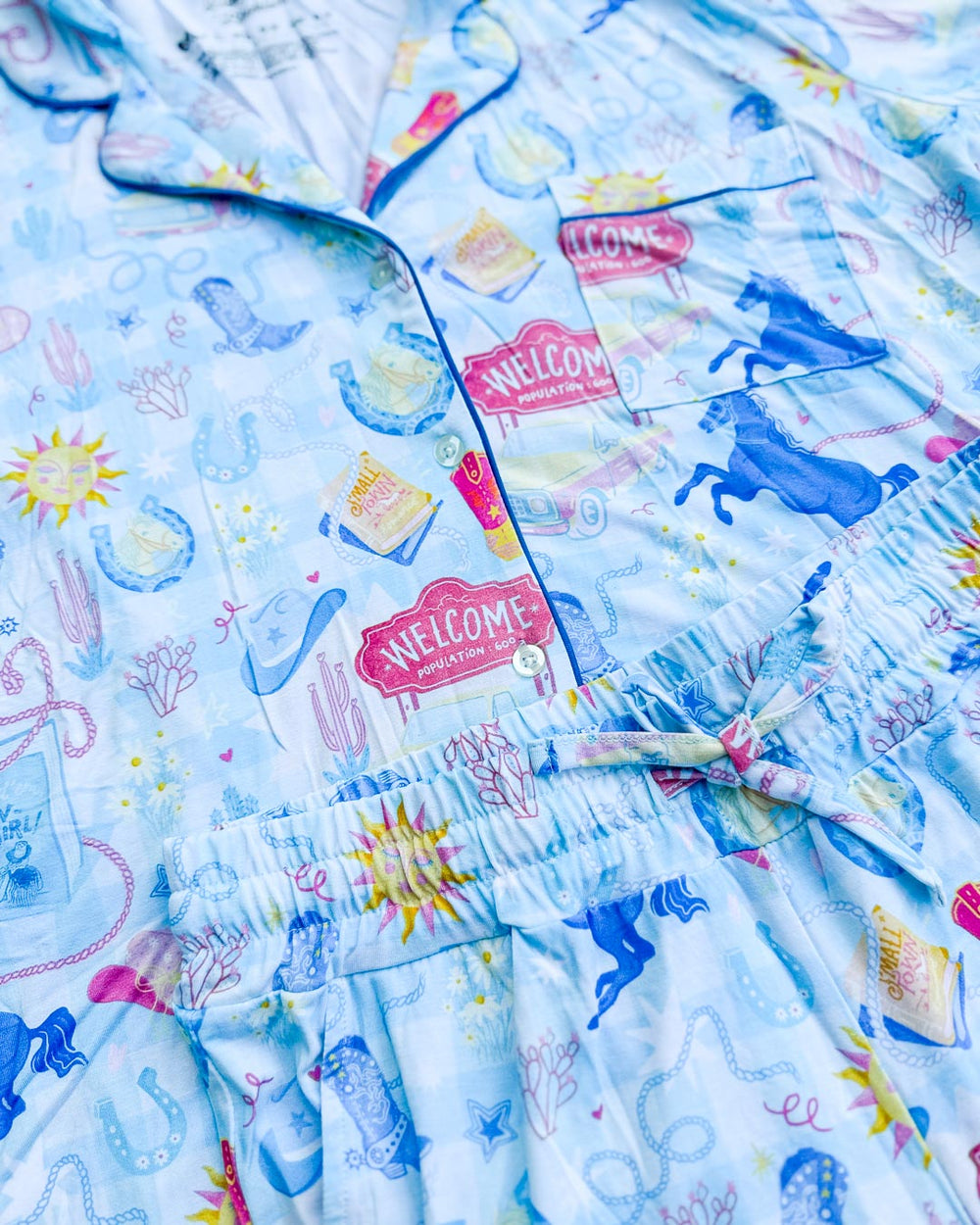 Close up of the cowboy romance pajamas set featuring cowboy hats, horses, lassos, horseshoes, cowboy boots, and more.