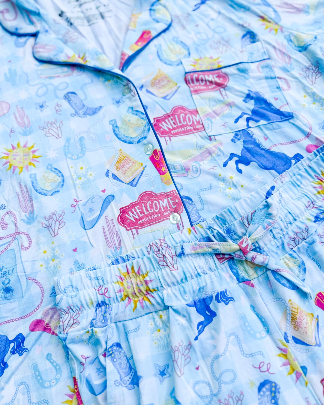 Close up of the cowboy romance pajamas set featuring cowboy hats, horses, lassos, horseshoes, cowboy boots, and more.