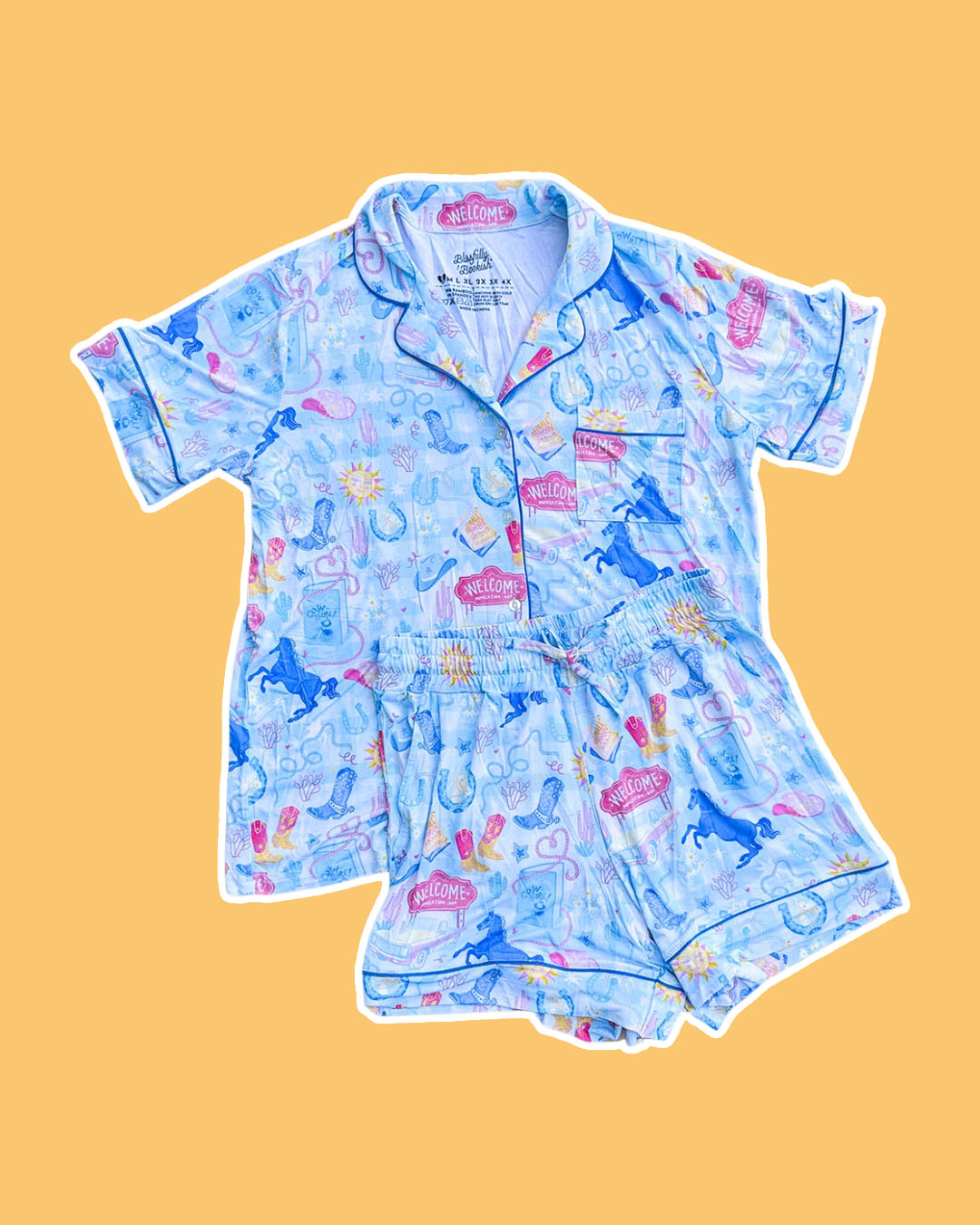 Cowboy romance pjs set with collared button down shirt, a pocket, and a stretchy waistband with a printed design featuring cowboy boots, horseshoes, horses, books, lassos, and more.