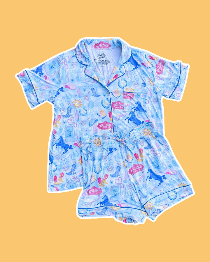 Cowboy romance pjs set with collared button down shirt, a pocket, and a stretchy waistband with a printed design featuring cowboy boots, horseshoes, horses, books, lassos, and more.