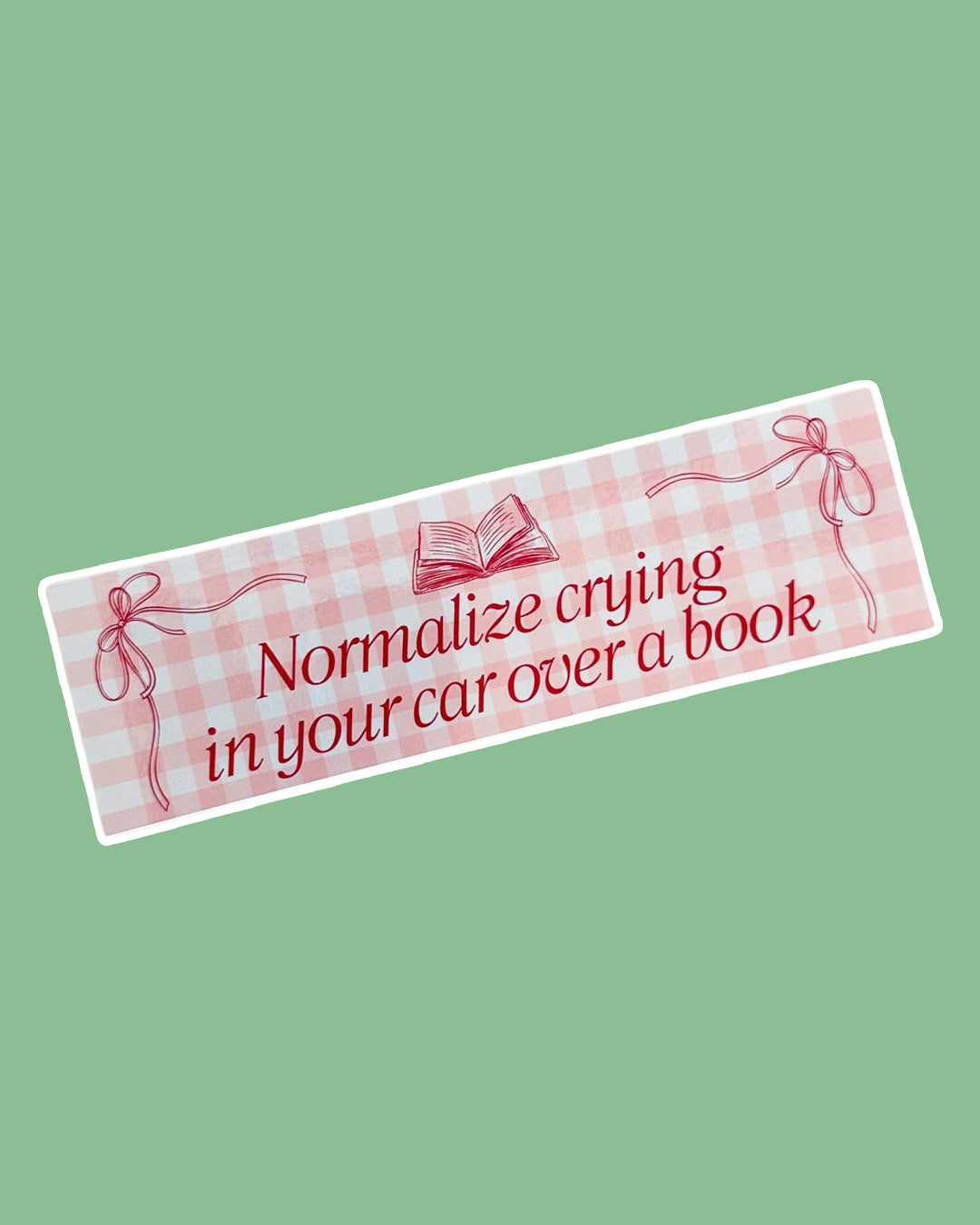 Pink, girly bookish bumper sticker with the phrase 'normalize crying in your car over a book' adorned with little bows in the corners and an open book at the top.
