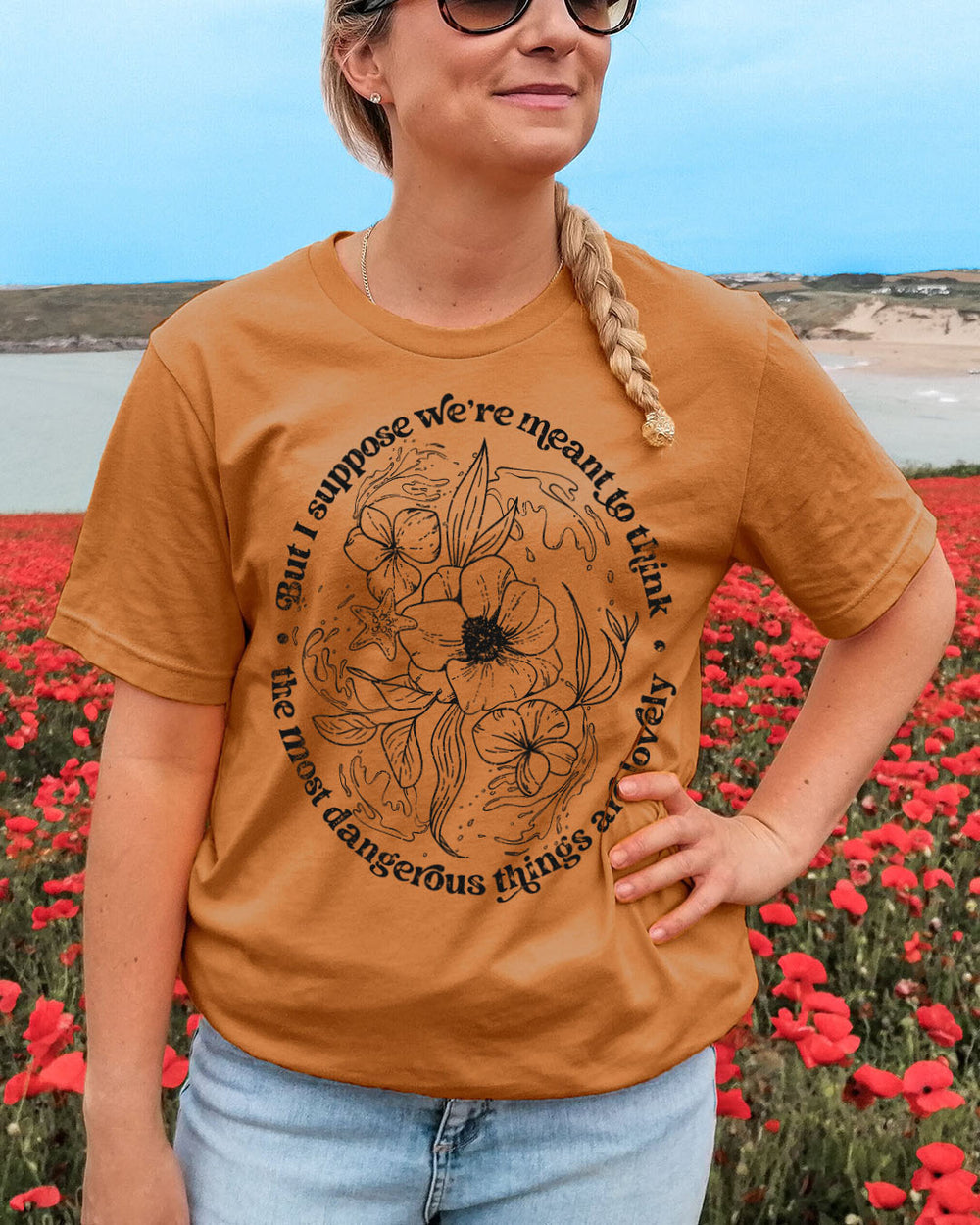 Bookish shirt with the quote 'But I suppose we're meant to think the most dangerous things are lovely' from Bring Me Your Midnight by Rachel Griffin with a flower and water design in the middle.