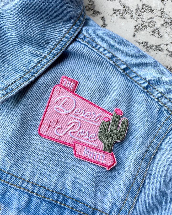 Emily Henry patch for People We Meet on Vacation fans featuring a welcome sign for The Desert Rose Motel in pink featuring stars and a cactus.