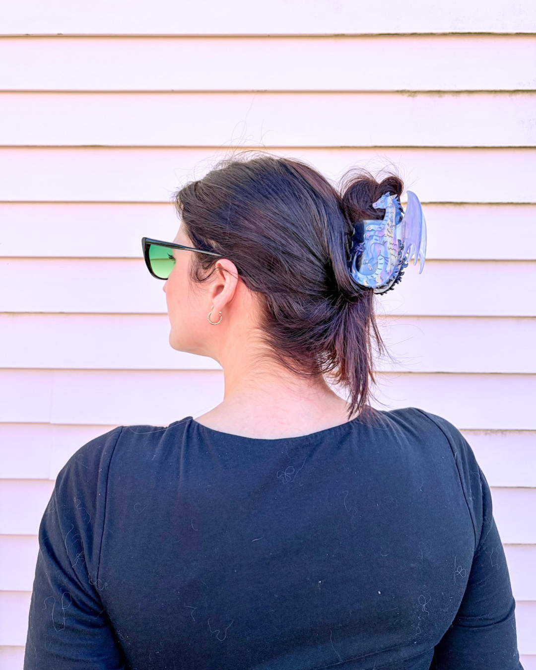 Woman with dark hair with her head turned to the side, showing off a fantasy hair claw clip for book lovers, featuring an iridescent purple dragon holding her hair up against a pinkish background.