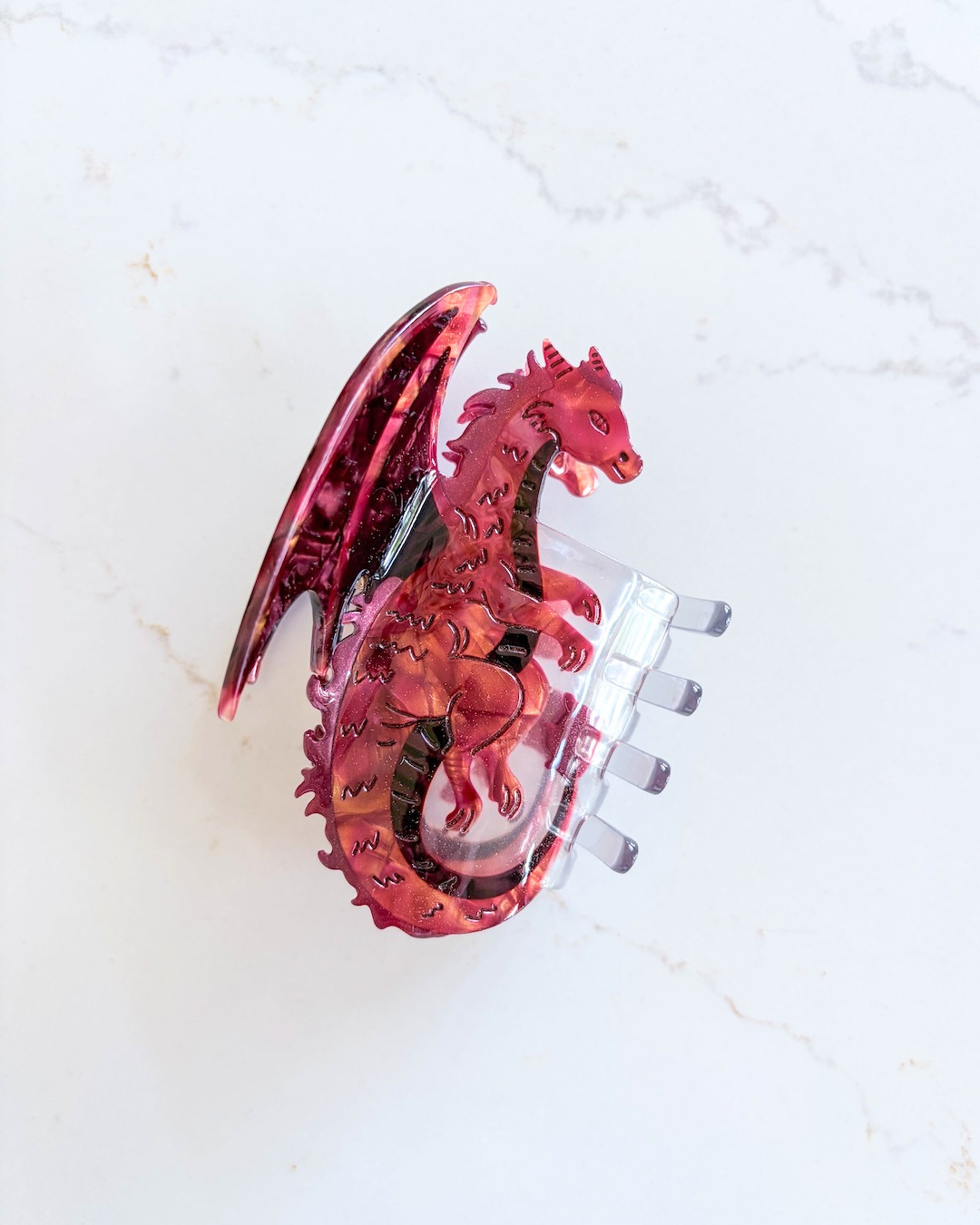 Red dragon hair claw clip for fantasy fans on a white marble background.