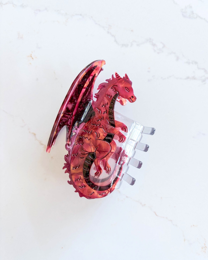Red dragon hair claw clip for fantasy fans on a white marble background.