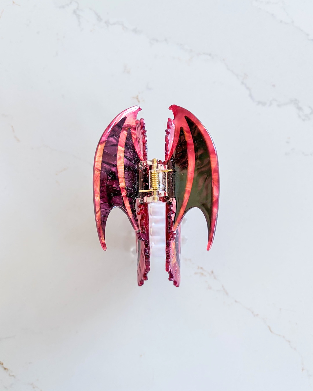 Marbled wings of a dragon hair clip for fantasy readers featuring an array of red and orange colors on a white marble background.