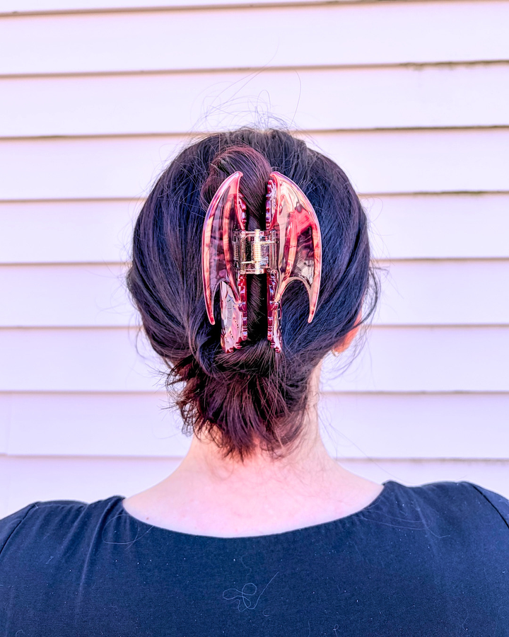 Close up of the dragon claw clip holding up dark hair, featuring an iridescent red shine to the dragon.