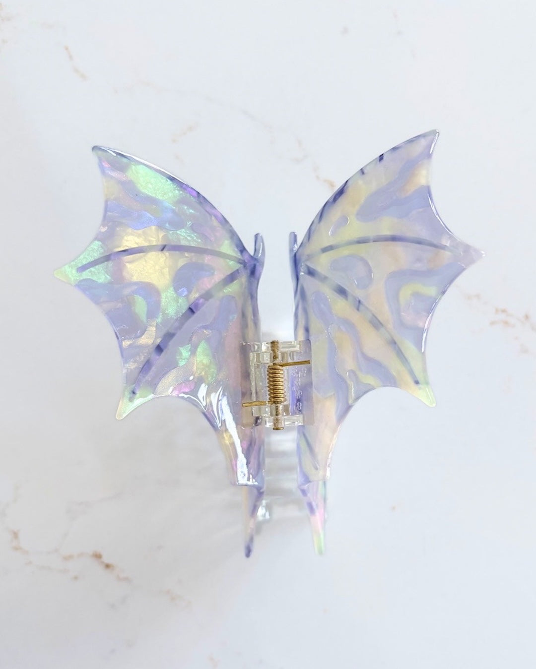 Iridescent purple dragon wing claw clip on a white marble background.