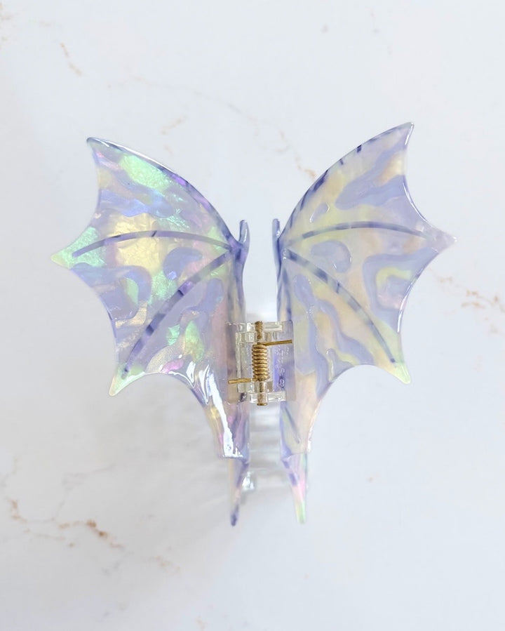 Iridescent purple dragon wing claw clip on a white marble background.