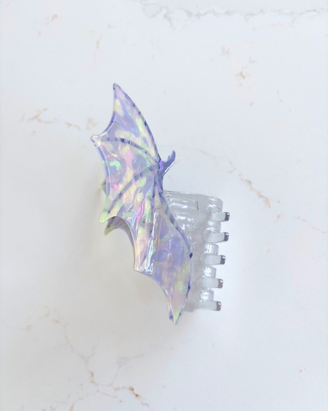Side view of the dragon wings claw clip featuring a wind spread wide in iridescent purple all on a white marble background.