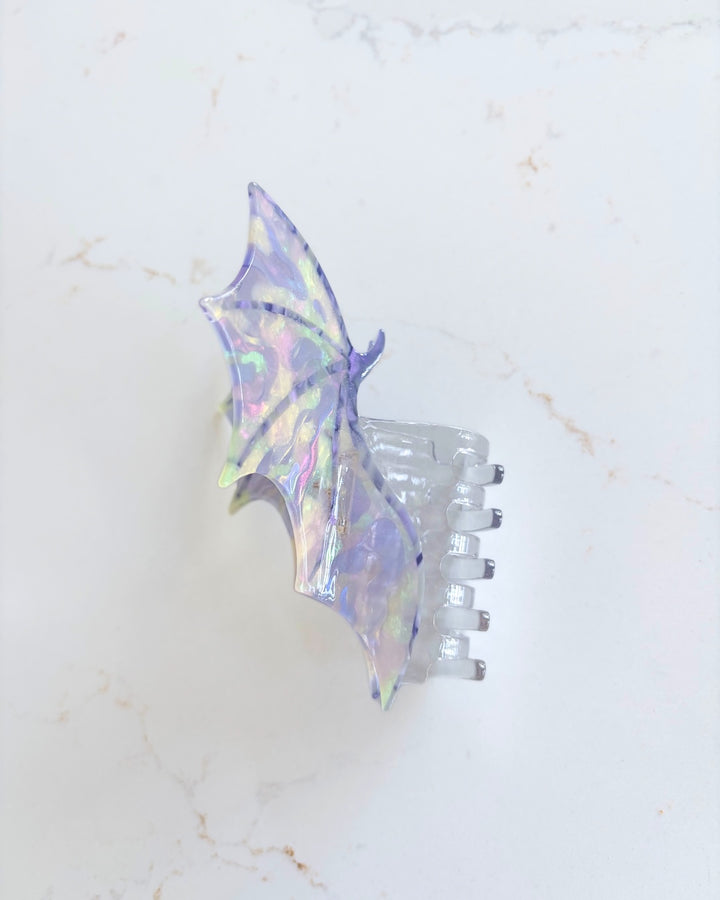 Side view of the dragon wings claw clip featuring a wind spread wide in iridescent purple all on a white marble background.