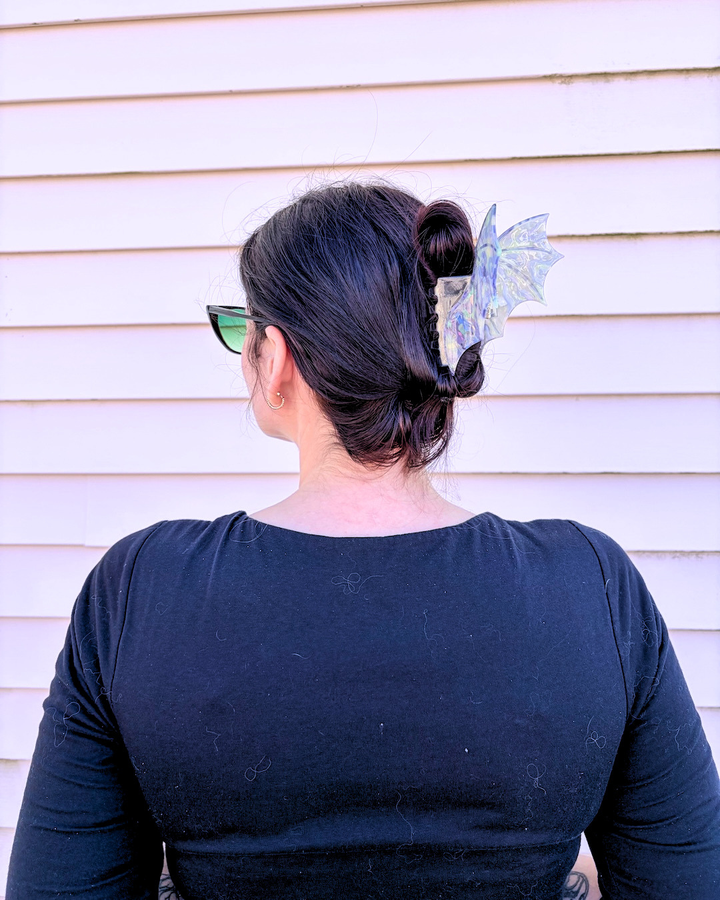 Woman with her head turned to the side, showing off a light purple dragon wing hair clip for fantasy fans on a pinkish background.