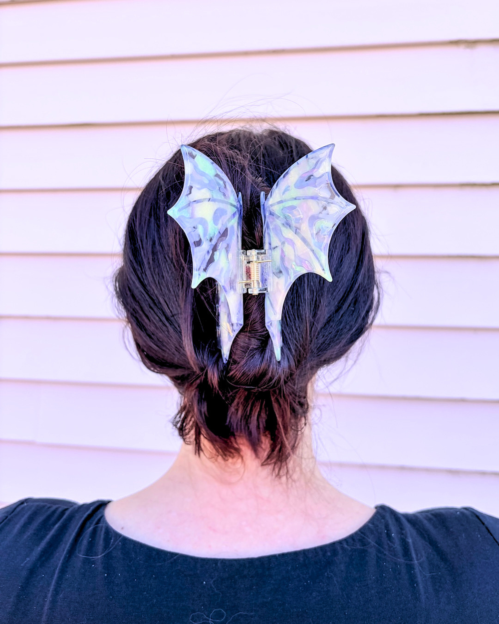 Woman wearing a dragon wing claw clip for fantasy lovers, featuring purple, iridescent dragon wings spread wide on a pinkish background.