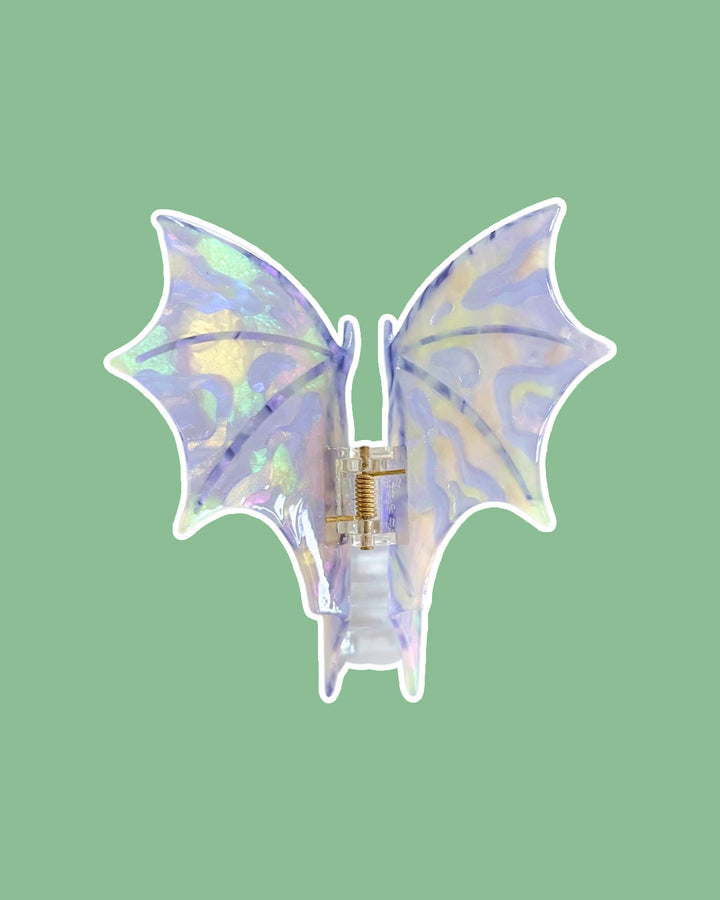 Purple, iridescent dragon wing hair clip against a green background.
