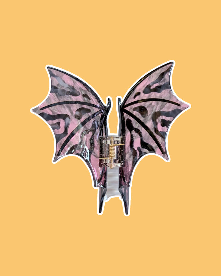 Pink and black dragon wing hair clip against a yellow background.
